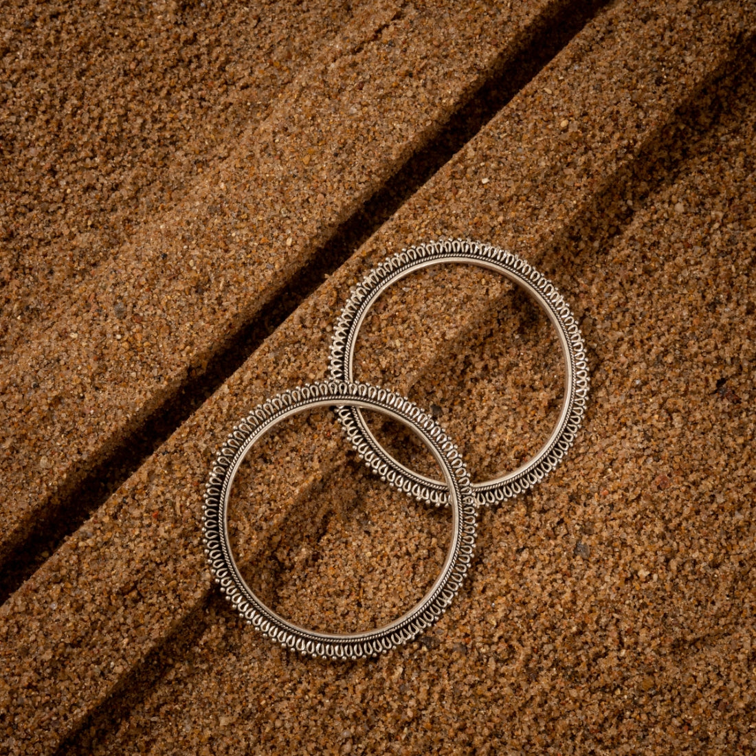 Set of two oxidized silver bangles featuring a delicate floral design with filigree details.