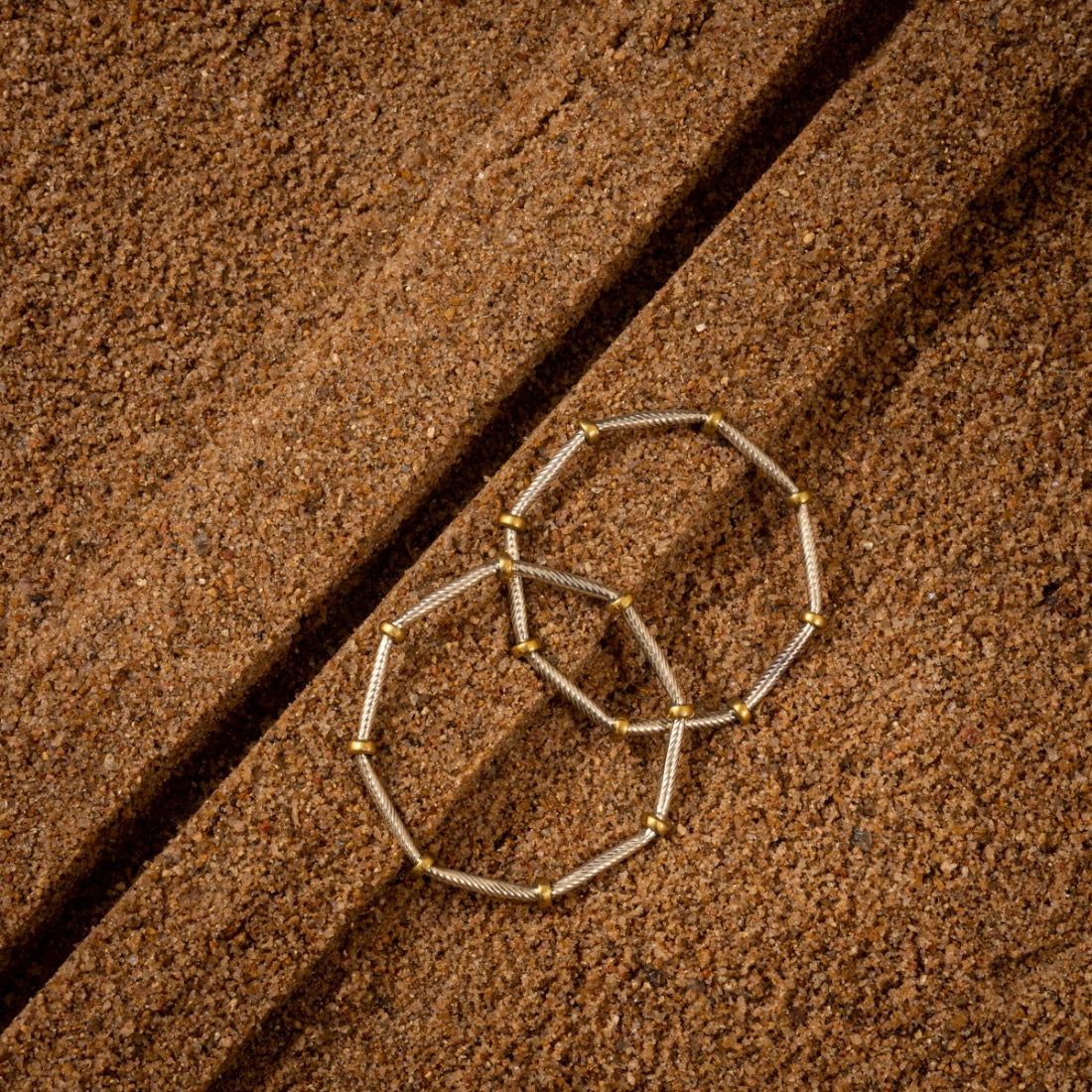 Set of two silver bangles featuring a two-tone finish with gold-plated rings and a unique octagonal shape on a grainy background.