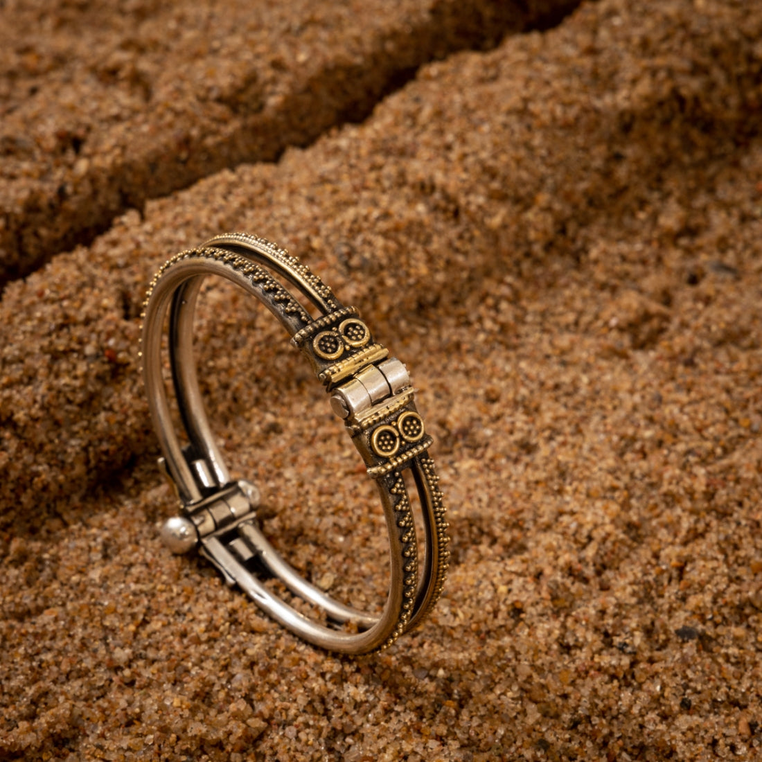 Modern two-tone silver cuff bracelet featuring bold tribal design on a grainy background.