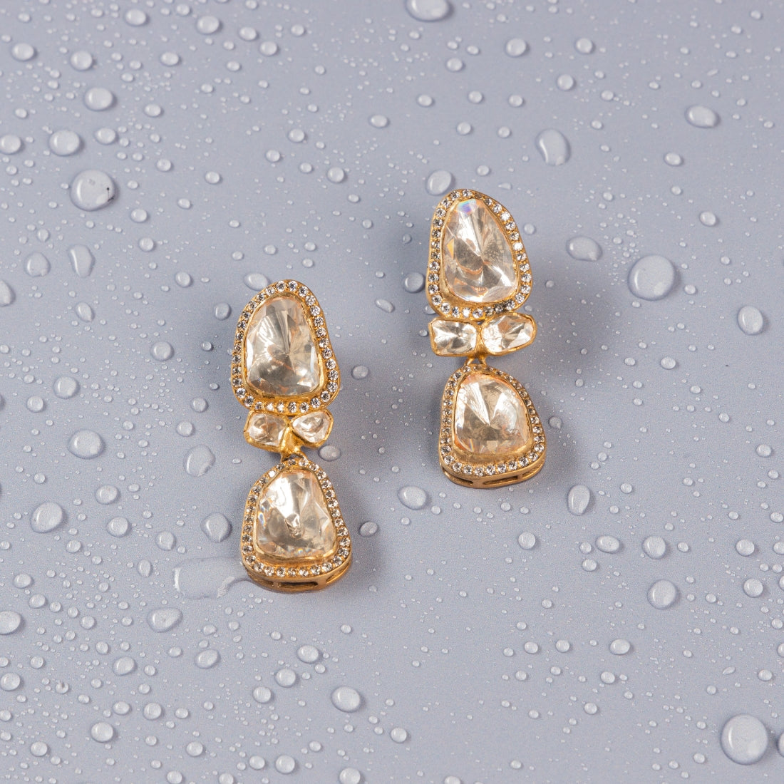 Silver drop earrings featuring various sized moissanite stones surrounded by CZ stones in prong settings. The earrings are finished with a gold plating.