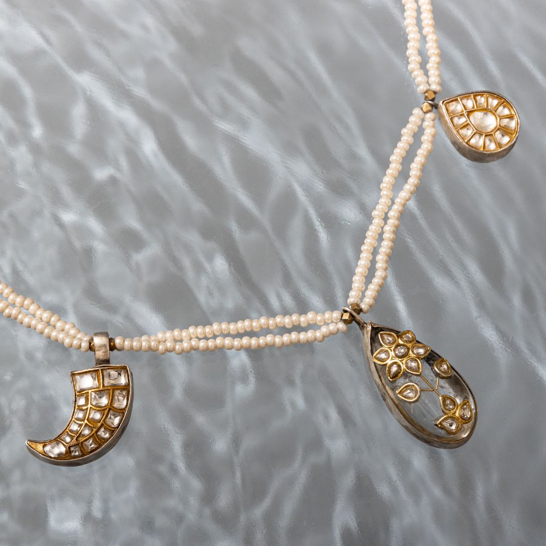 Jadau long necklace featuring a grey center stone with polki detailing, flanked by claw and pear-shaped charms. Delicate pearl strands complete the design.