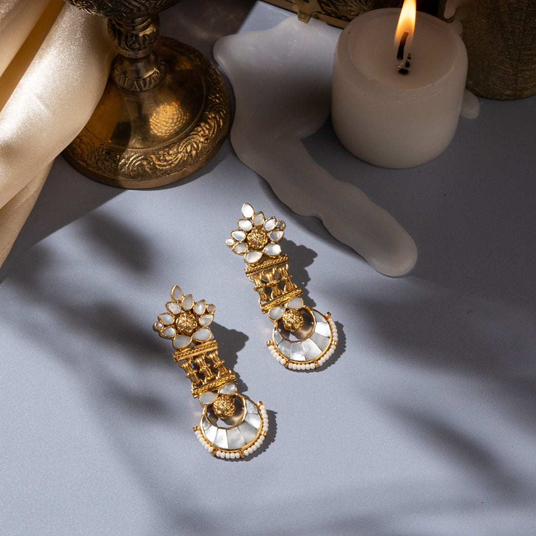 Silver statement earrings featuring a floral motif with mother-of-pearl inlay, a crescent moon motif with mother-of-pearl inlay, and bold tribal-inspired metal links. Cascading pearls hang below the crescent moon motif.